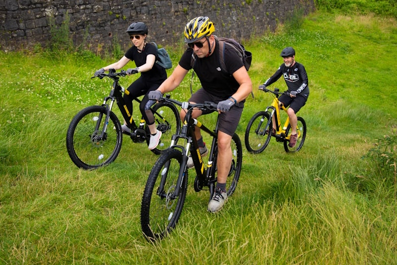 Three people riding Mark2 Scrambler C E-Bikes up a steep grassy hill
